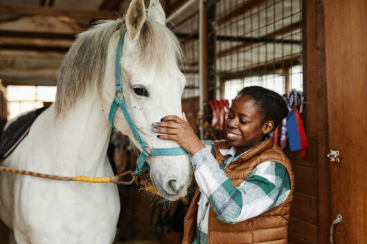 A young woman smiling and petting a horse.